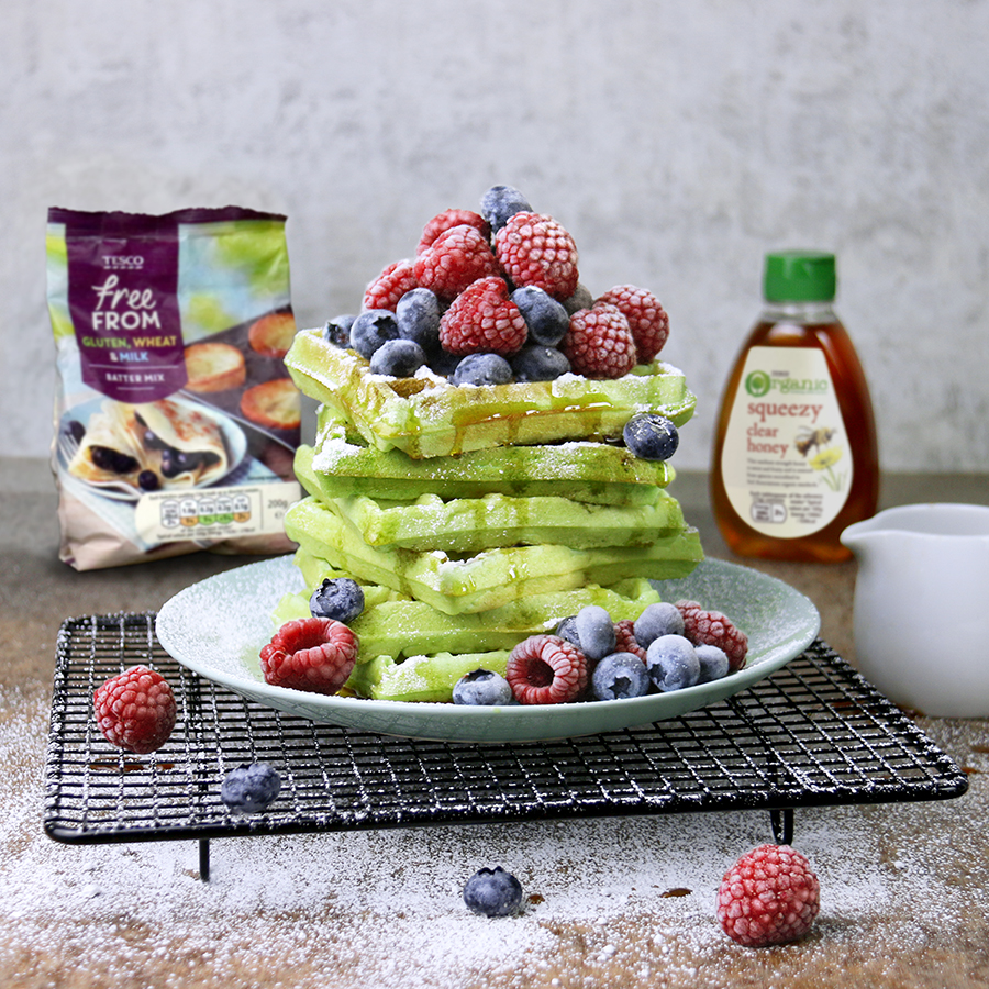 A stack of pandan waffles topped with berries, accompanied by Tesco products used to make the dish